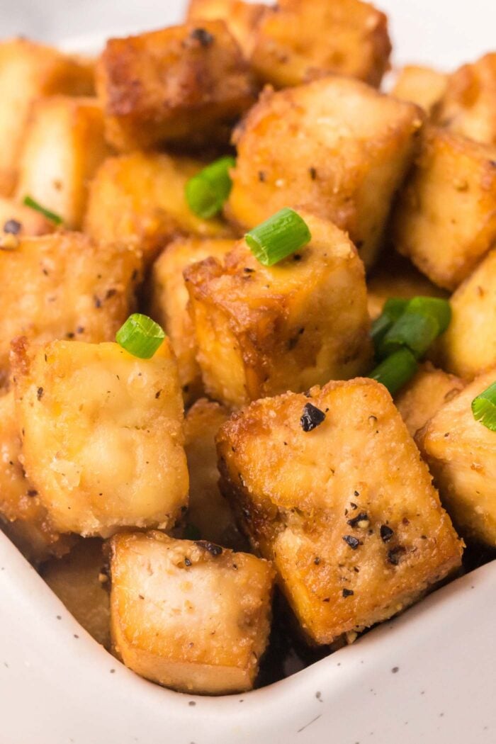 Close up of crispy tofu cubes sprinkled with green onion in a bowl.