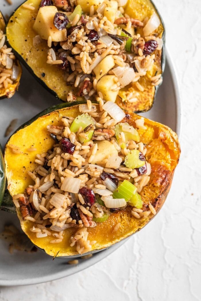 Two halves of roasted acorn squash stuffed with rice, cranberries, pecans, apple and celery.