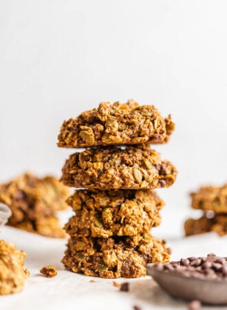 Stack of 4 sweet potato cookies with a small dish of chocolate chips in foreground and more cookies in background.
