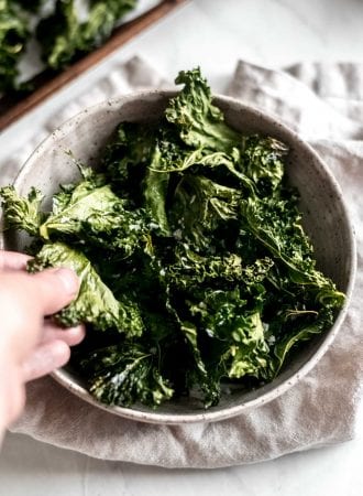 Hand reaching for some baked crispy kale chips.