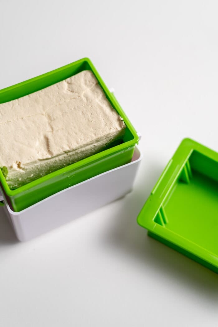 A block of tofu in a rectangular box tofu press.