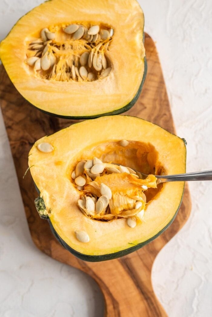 Two acorn squash halves with the spoon scooping out the seeds.
