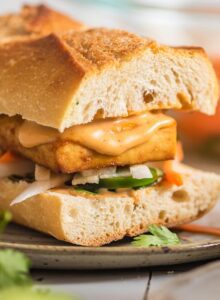 Close up of a tofu bahn mi sandwich with spicy mayo and pickled veggies on a plate.