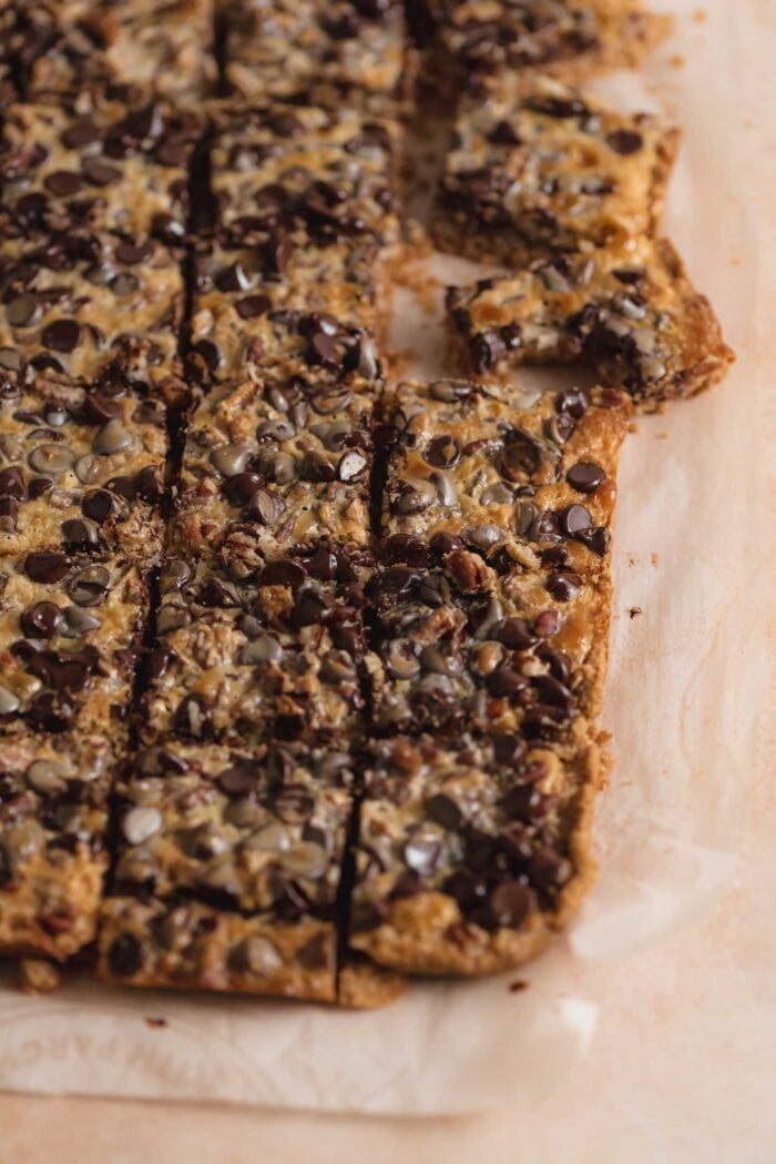 A batch of seven layer magic cookie bars made with pecans, coconut and chocolate chips cut into squares with one bar pulled aside with a bite out of it.