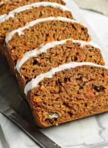 Sliced vegan carrot cake banana bread topped with cream cheese frosting on a marble cutting board.