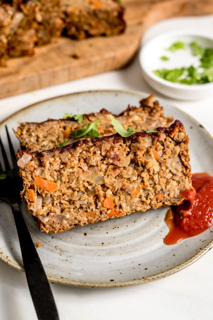 Two slices of vegetarian chickpea meatloaf on a plate with ketchup. Fork rests on plate.