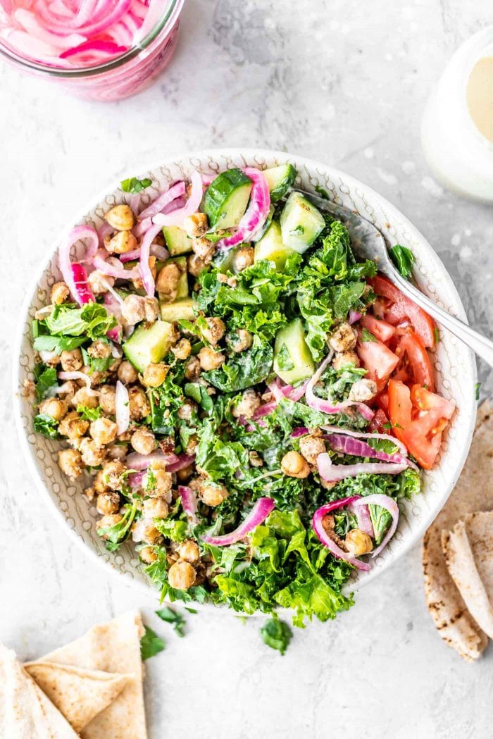 Salad with chickpeas, kale, tomato, parsley, red onion, tahini sauce and cucumber.