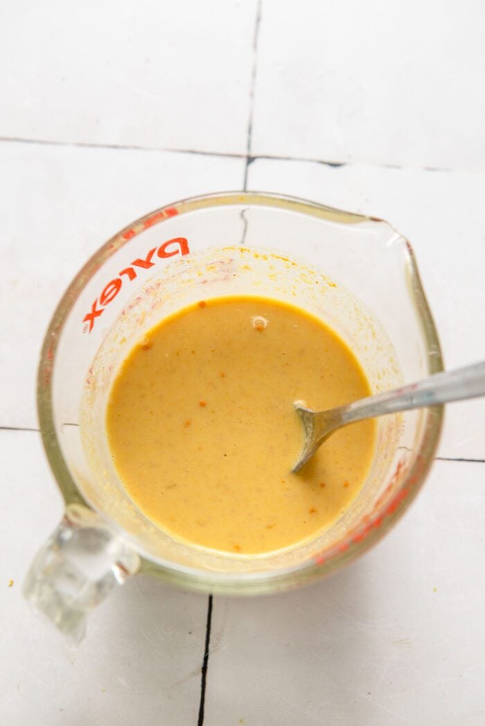 Creamy, yellow sauce in a glass measuring up with spoon in it.