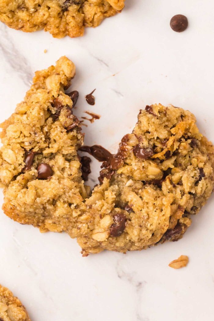 An almond flour oatmeal chocolate chip cookie broken in half so you can see some of the melted chocolate chips inside.