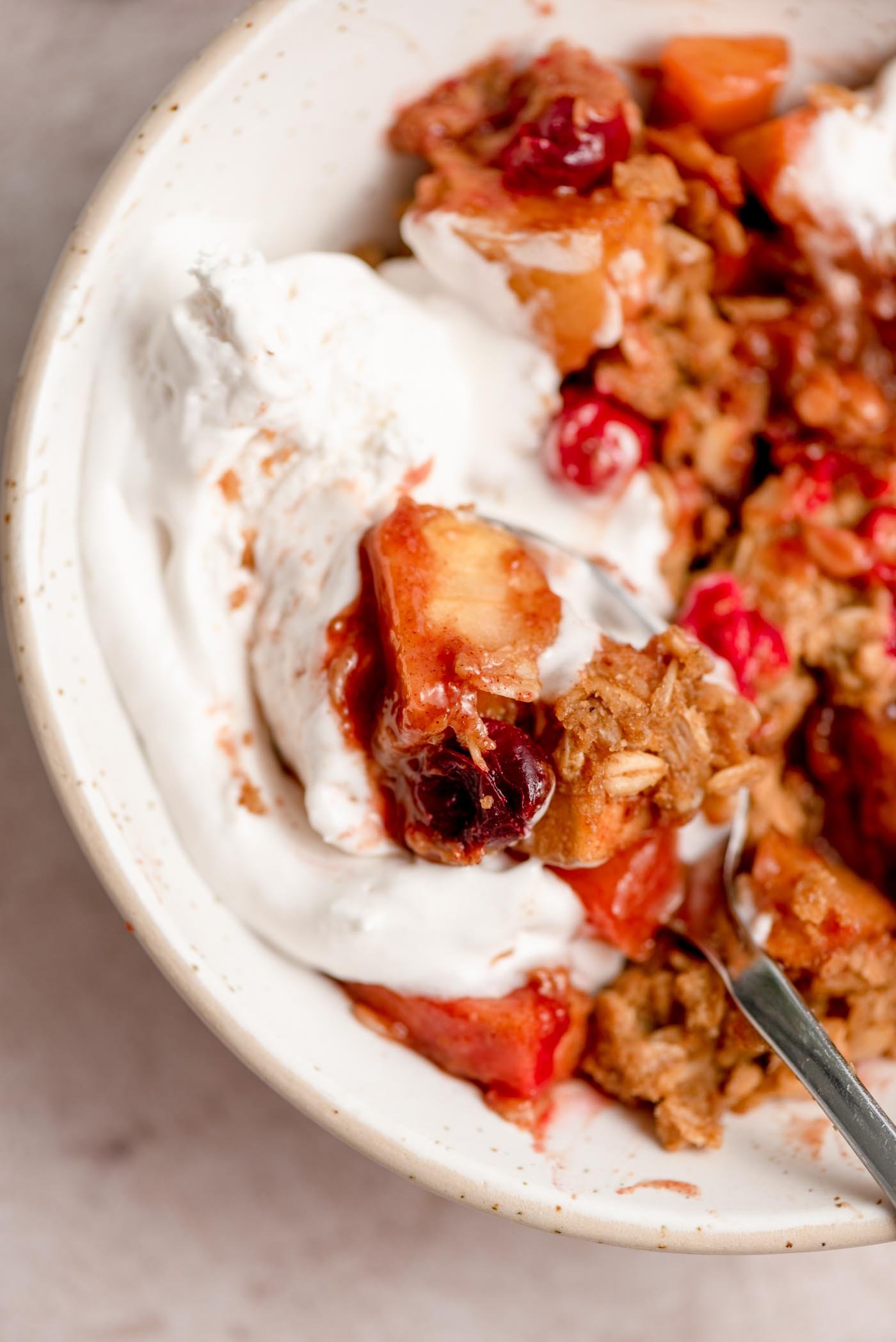 A bowl of cranberry apple crisp with whipped cream on top and a spoon in the bowl.