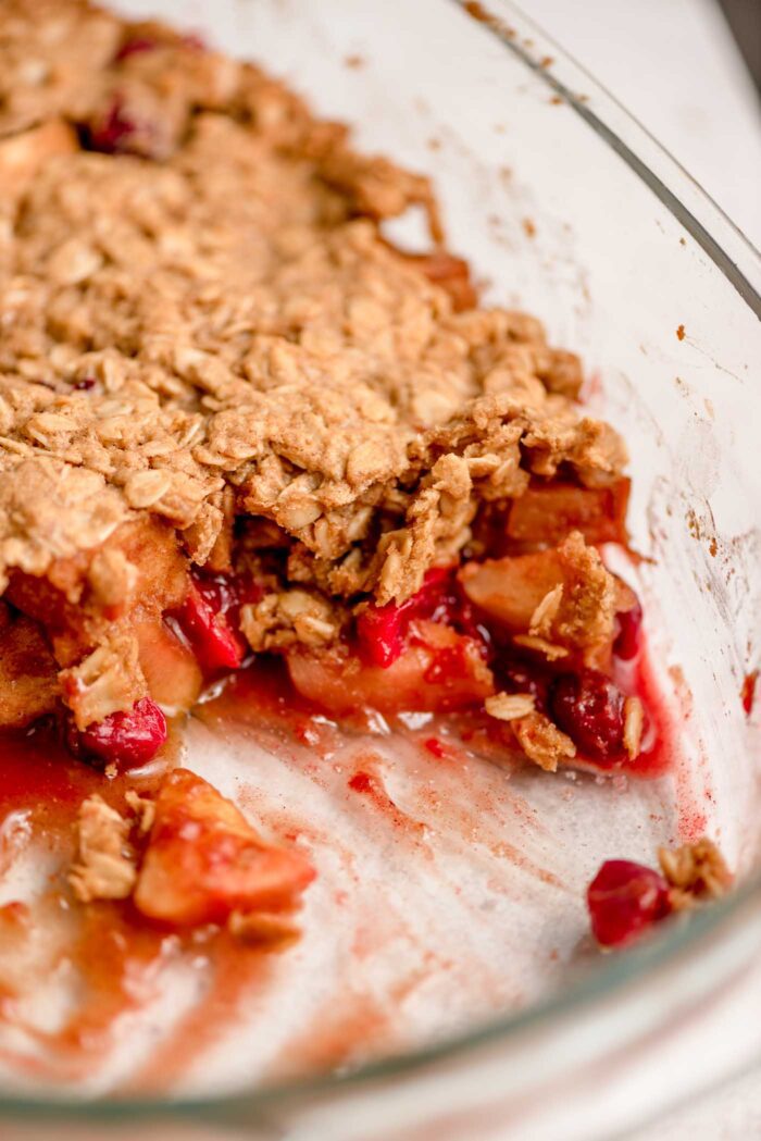 Apple cranberry crisp with a scoop out of it so you can see the apple cranberry filling and oatmeal crumble topping in a baking dish.