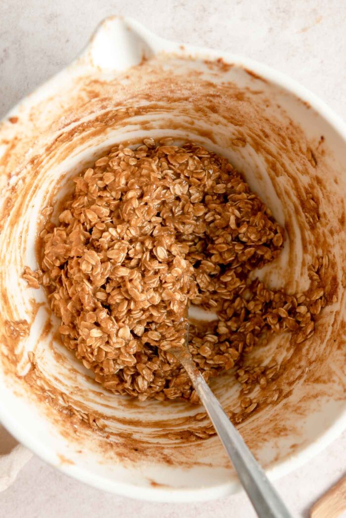 Oatmeal crumble topping mixture mixed up in a mixing bowl with a spoon in it.