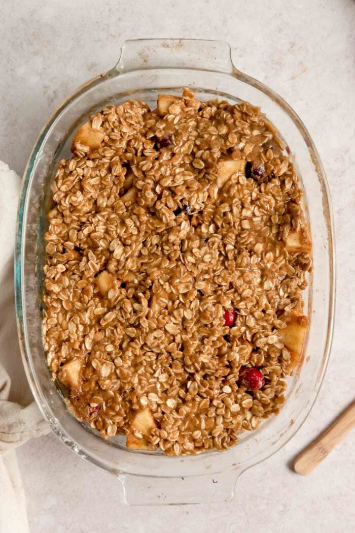 An apple cranberry crumble in a glass oval baking dish before going in the oven.