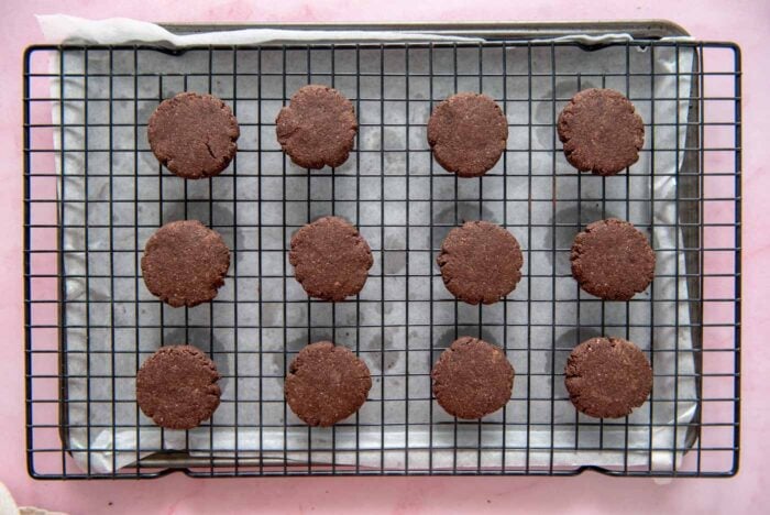 12 small round chocolate cookies on a cooling rack.