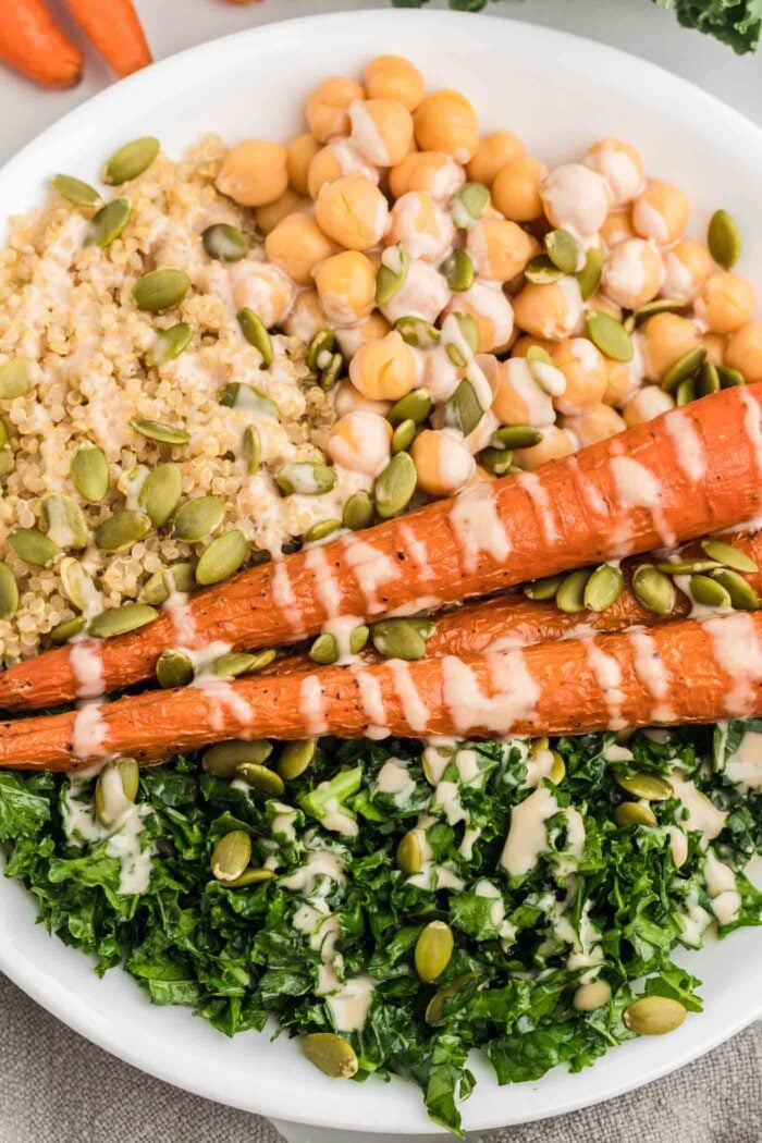 Quinoa, kale, chickpeas and whole roasted carrots topped with tahini sauce in a bowl.