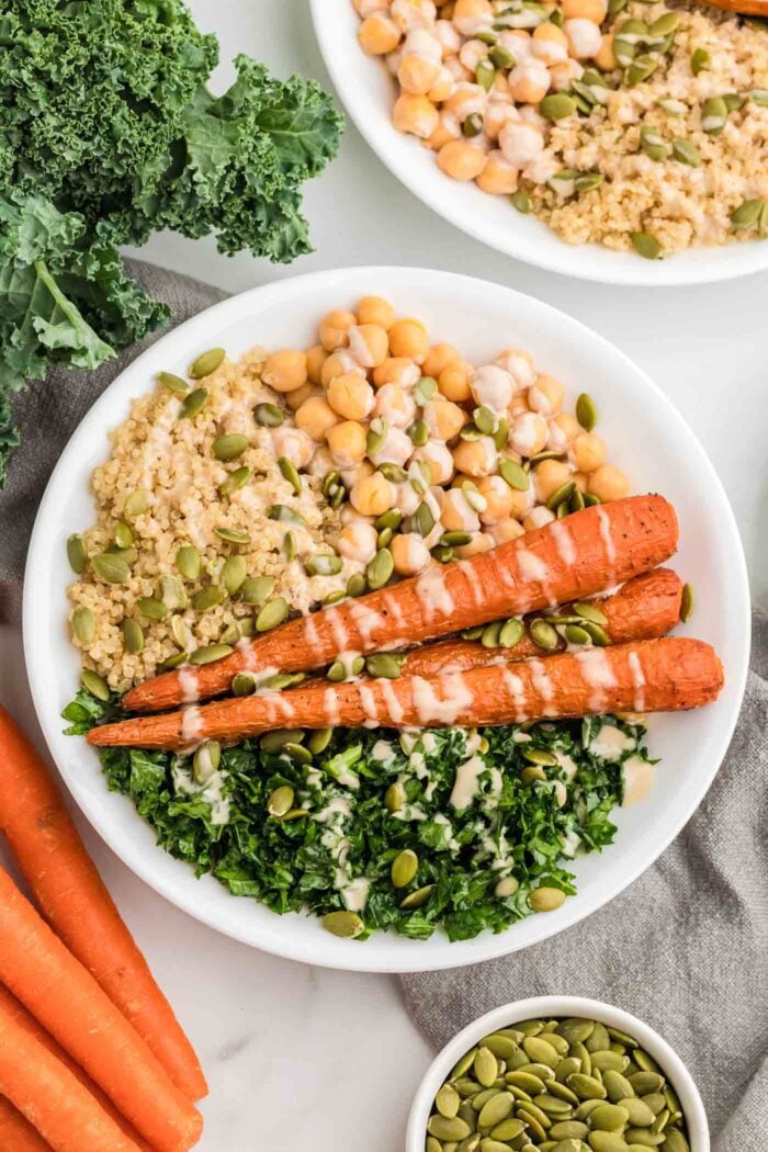 Healthy bowl with whole roasted carrots, quinoa, kale, pumpkin seeds and tahini dressing drizzled over top.