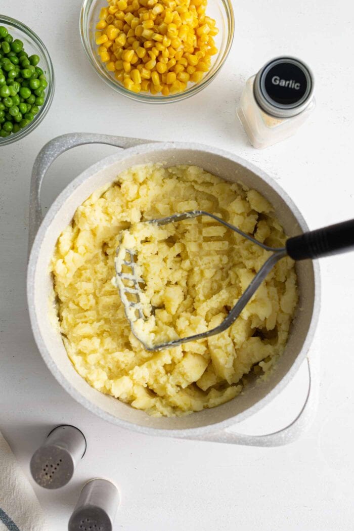 Mashed yellow potatoes in a pot with a masher.