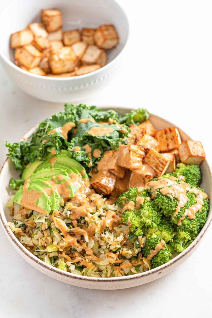 Bowl with cabbage, avocado, tofu, onion, kale and broccoli, topped with sauce.