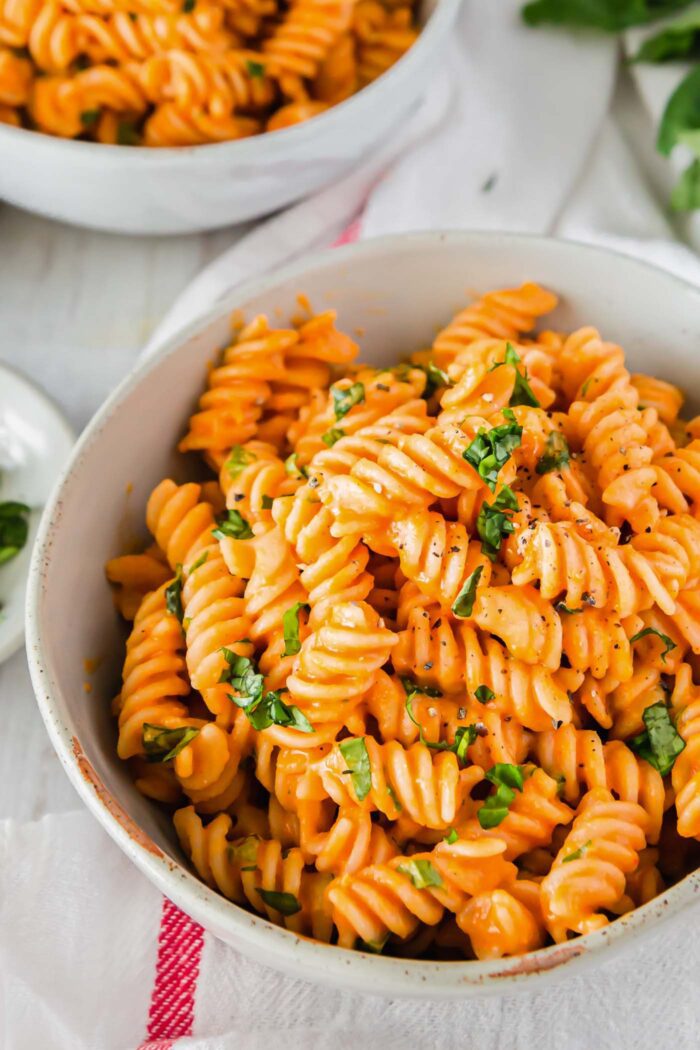 A bowl of vegan roasted red pepper pasta topped with chopped fresh herbs.