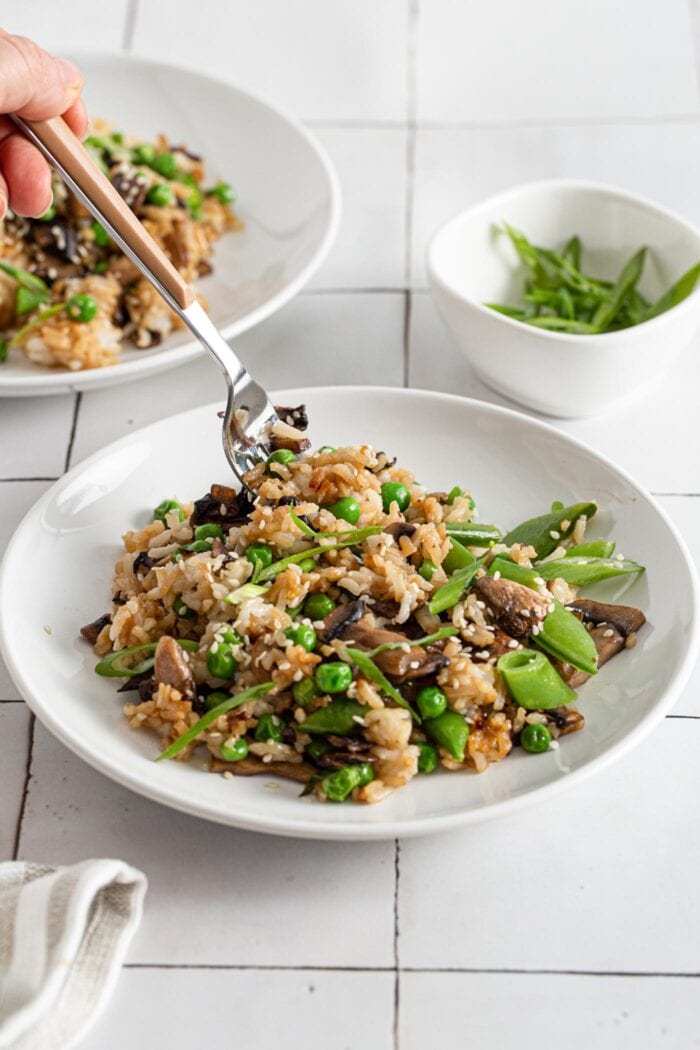 Hand with a fork taking a forkful of vegan mushroom fried rice.
