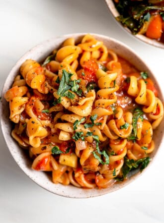 A bowl of rotini pasta with tomato sauce and vegetables.