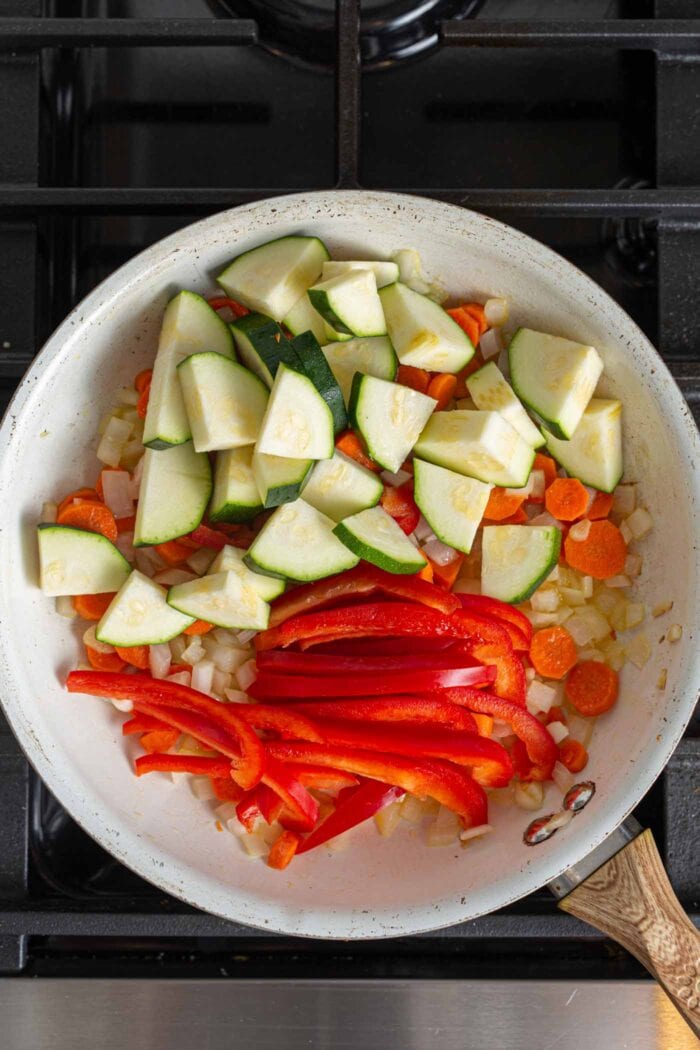 Diced zucchini and thinly sliced bell pepper in a skillet with carrot, onion and garlic.