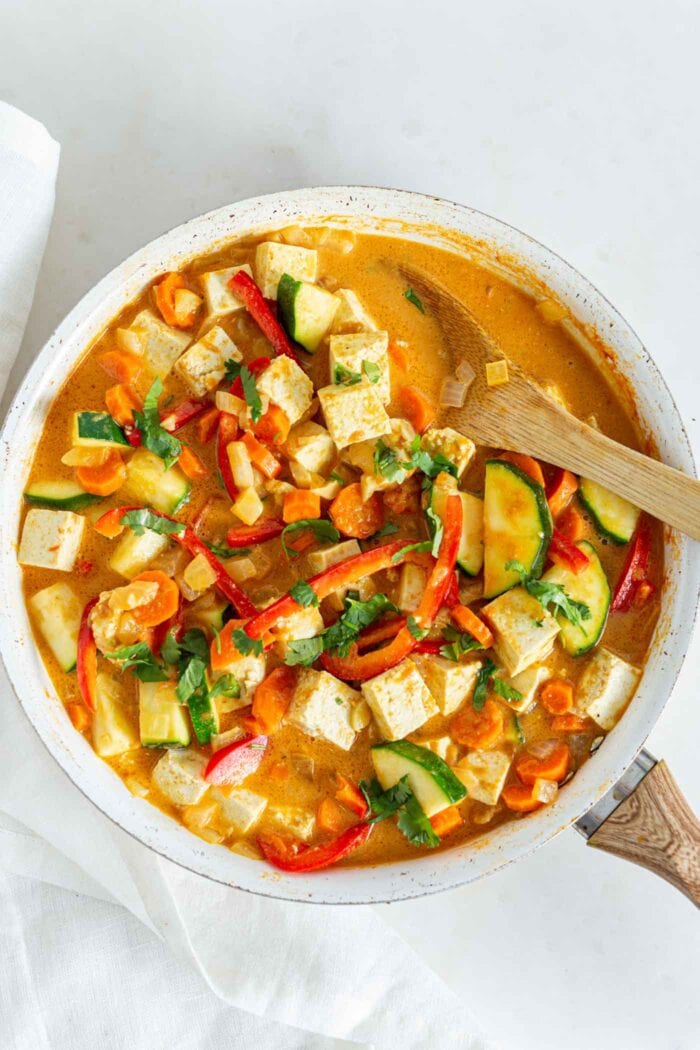 Thick and creamy vegetable curry with tofu in a skillet with a wooden spoon.