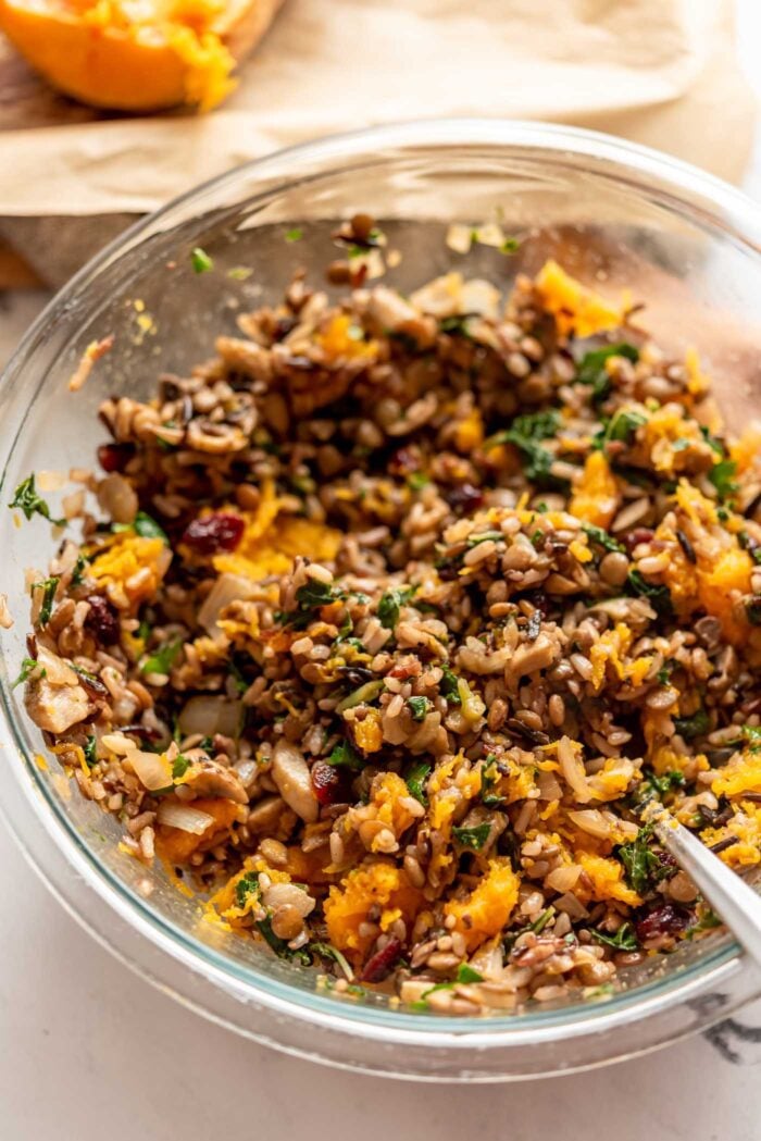 Wild rice, lentil, squash and kale mixed together in a glass mixing bowl.