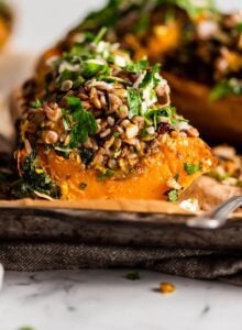 Sliced rice, lentil and kale stuffed butternut squash on a parchment paper-lined baking tray.