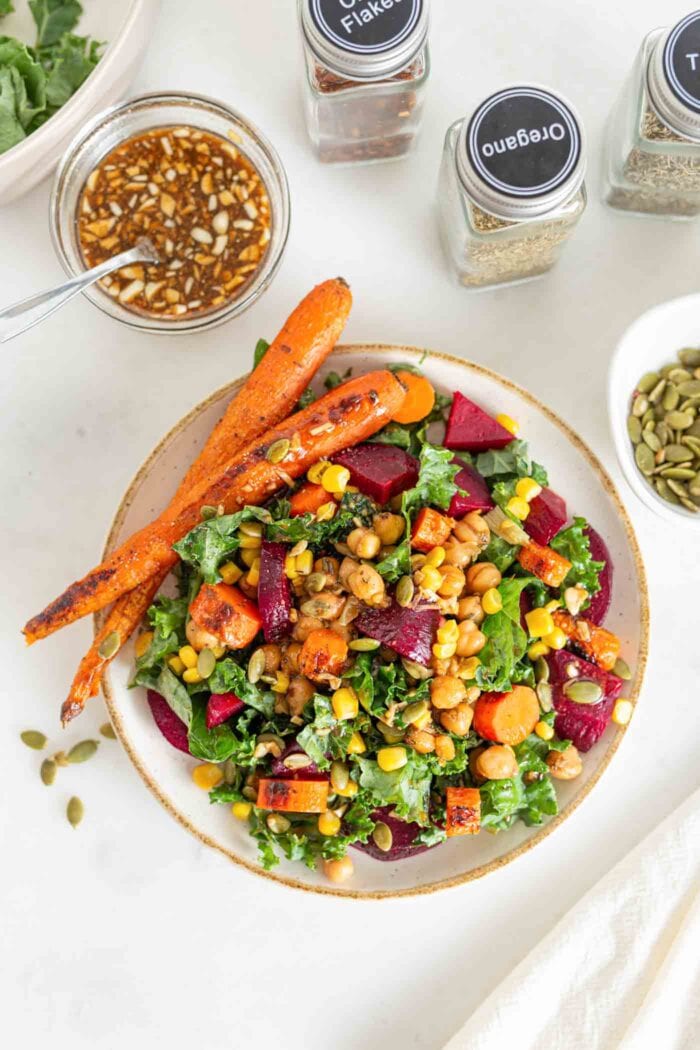 Bowl of kale salad with beet, corn, carrots and pumpkin seeds.