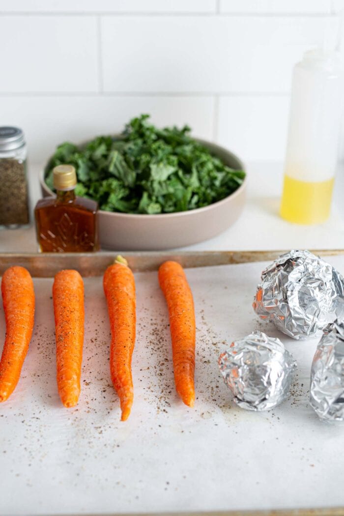 Whole carrots and foil wrapped beets on a baking tray lined with parchment paper.