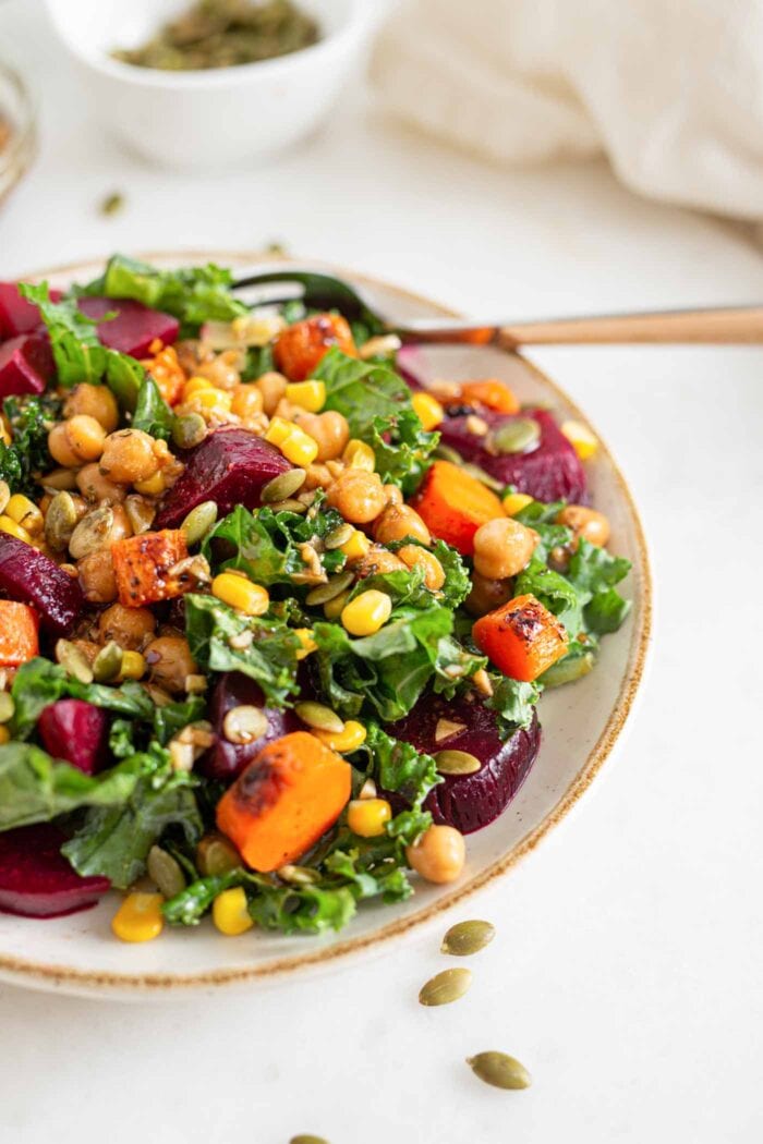 Bowl of kale salad with chickpeas, carrots, beets and corn.