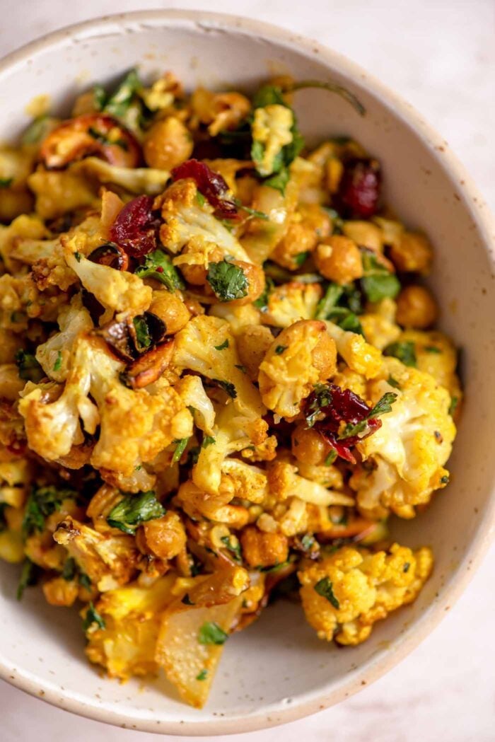 Close up overhead view of a small bowl of curried roasted cauliflower salad with onion slices, chickpeas and cranberries in a creamy curry dressing.
