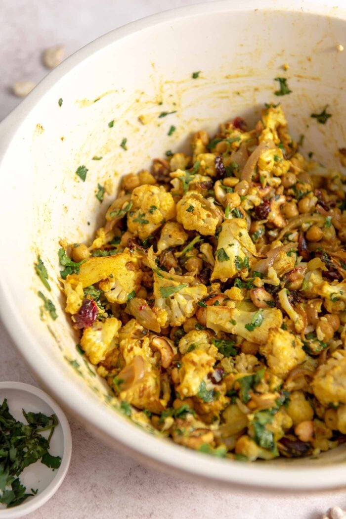 A curry roasted cauliflower salad with chickpeas, red onion, cilantro, cashews and cranberries in a large bowl.