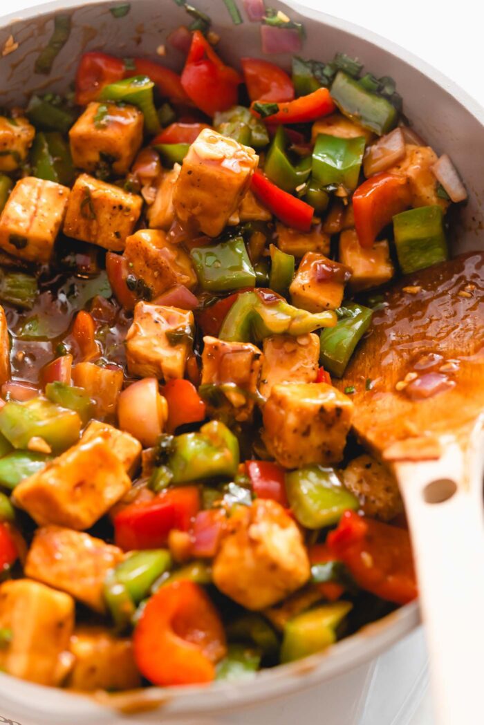 Sweet and sour tofu stir fry with bell peppers and onion cooking in a skillet.