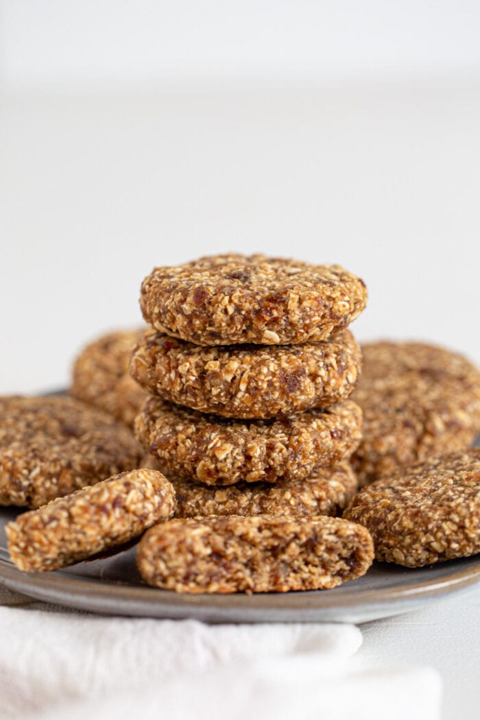4 oat date cookies stacked on a plate. More cookies sit around the stack.