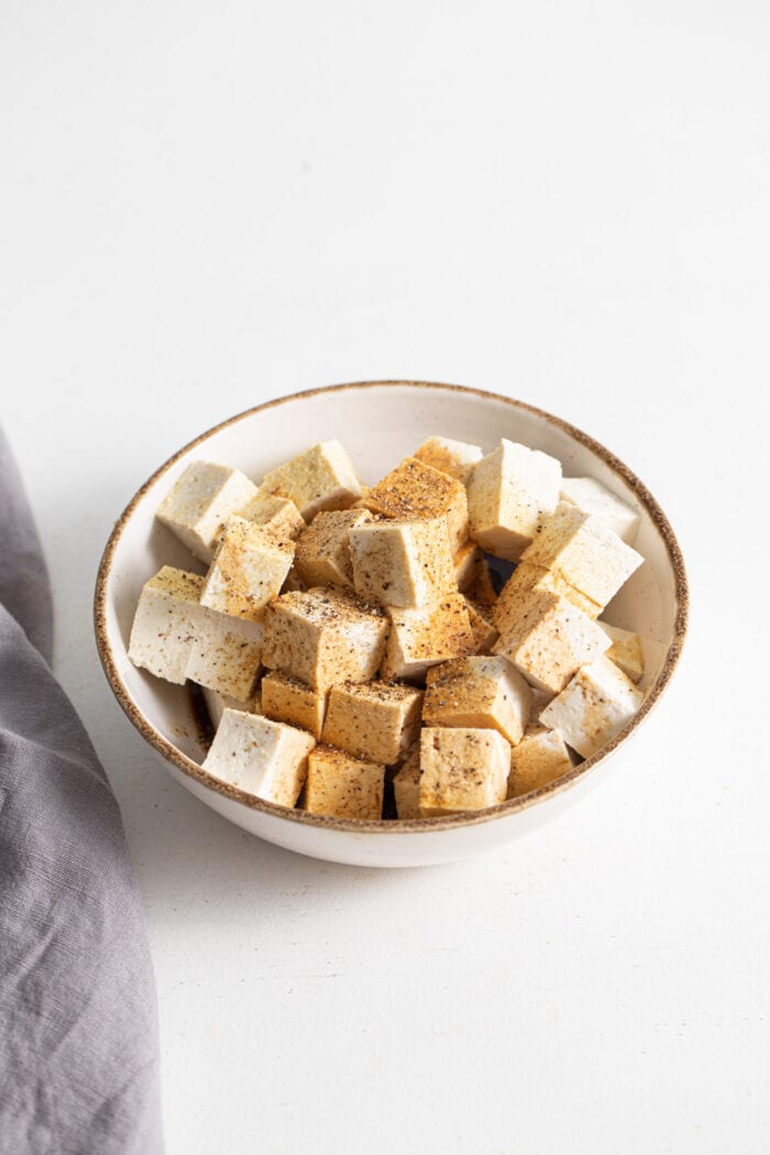 Cubed tofu in a bowl topped with garlic powder and black pepper.