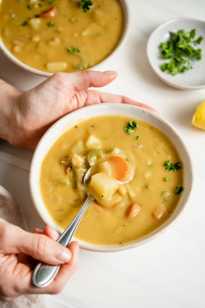 Hand using a spoon to take a spoonful of vegetable chowder out of a bowl.